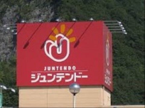 ホームセンターの看板である。赤っぽい色の看板に白で店舗名と店舗のロゴマークが描かれている。施設の近くにあるので買い物に便利だ。
