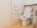トイレの壁には縦横つながった手すりが設置されている。便座の操作パネルの下にトイレットペーパーホルダーがついている。