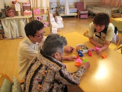テーブルで折り紙に勤しむ入居者様と、その様子を見守るスタッフたちの模様