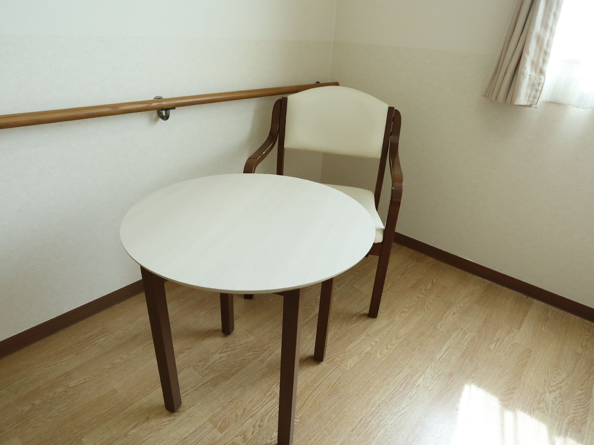 テーブルと椅子は、部屋の角に設置してある。それらの右側の壁には手すりがついている。また、窓からは陽が差し込んでいる。