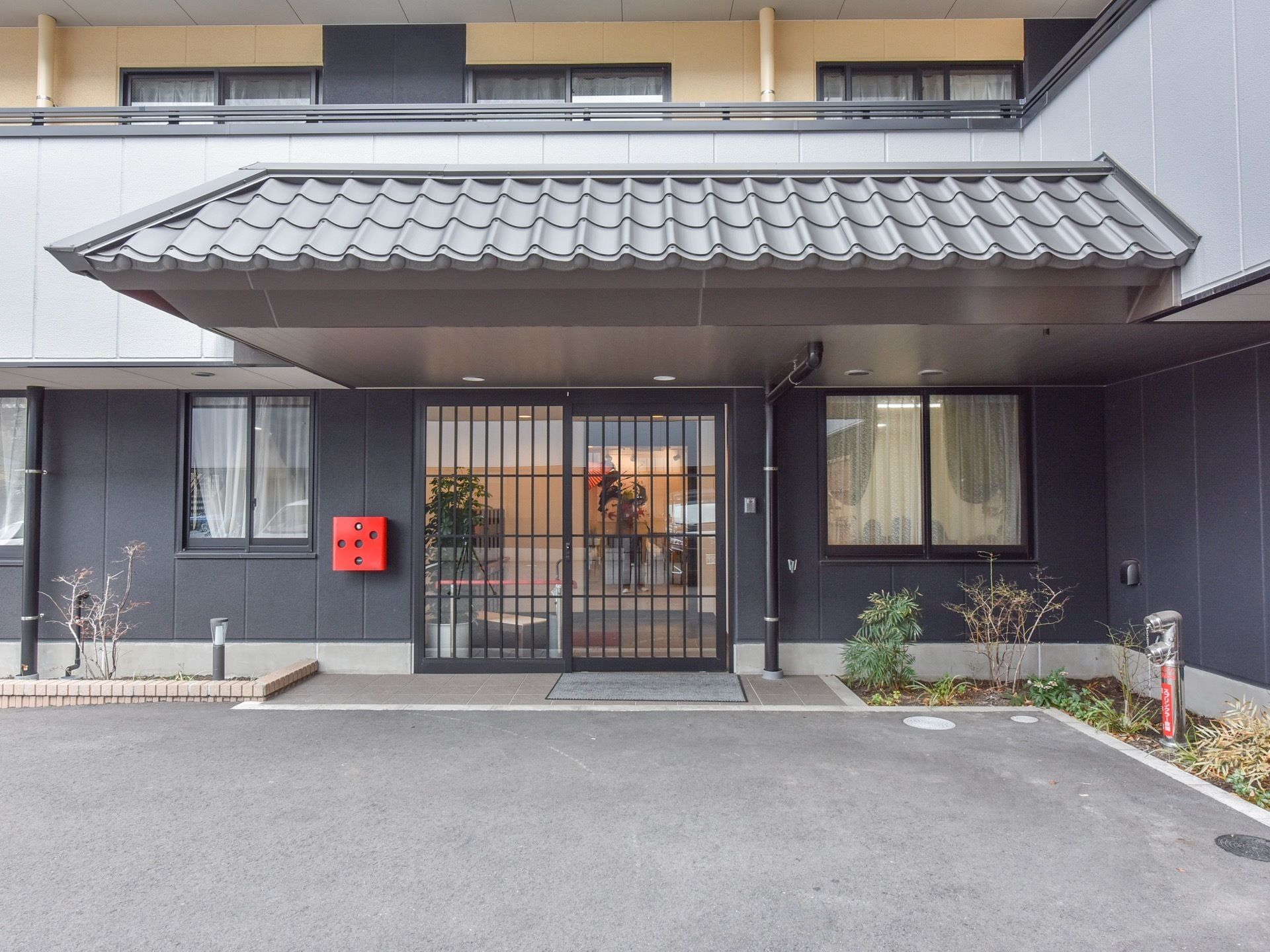 瓦屋根が特徴の、和テイストの玄関である。扉は館内の様子が分かるガラス張りで、外壁にはインターホンが設置されている。