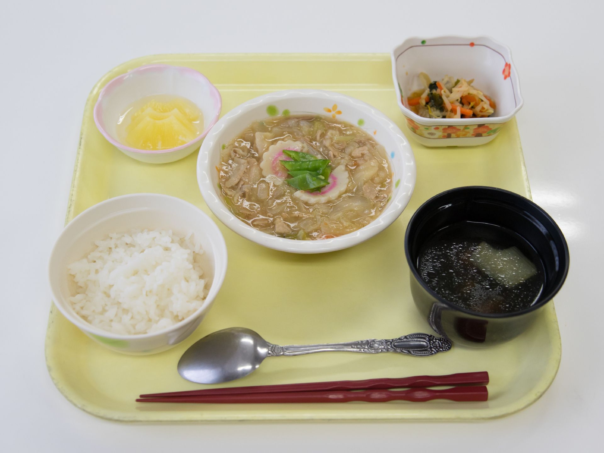 栄養バランスを考えた食事をトレイに乗せて提供している。食材は細かく刻まれている。箸とスプーンがトレイに乗っている。