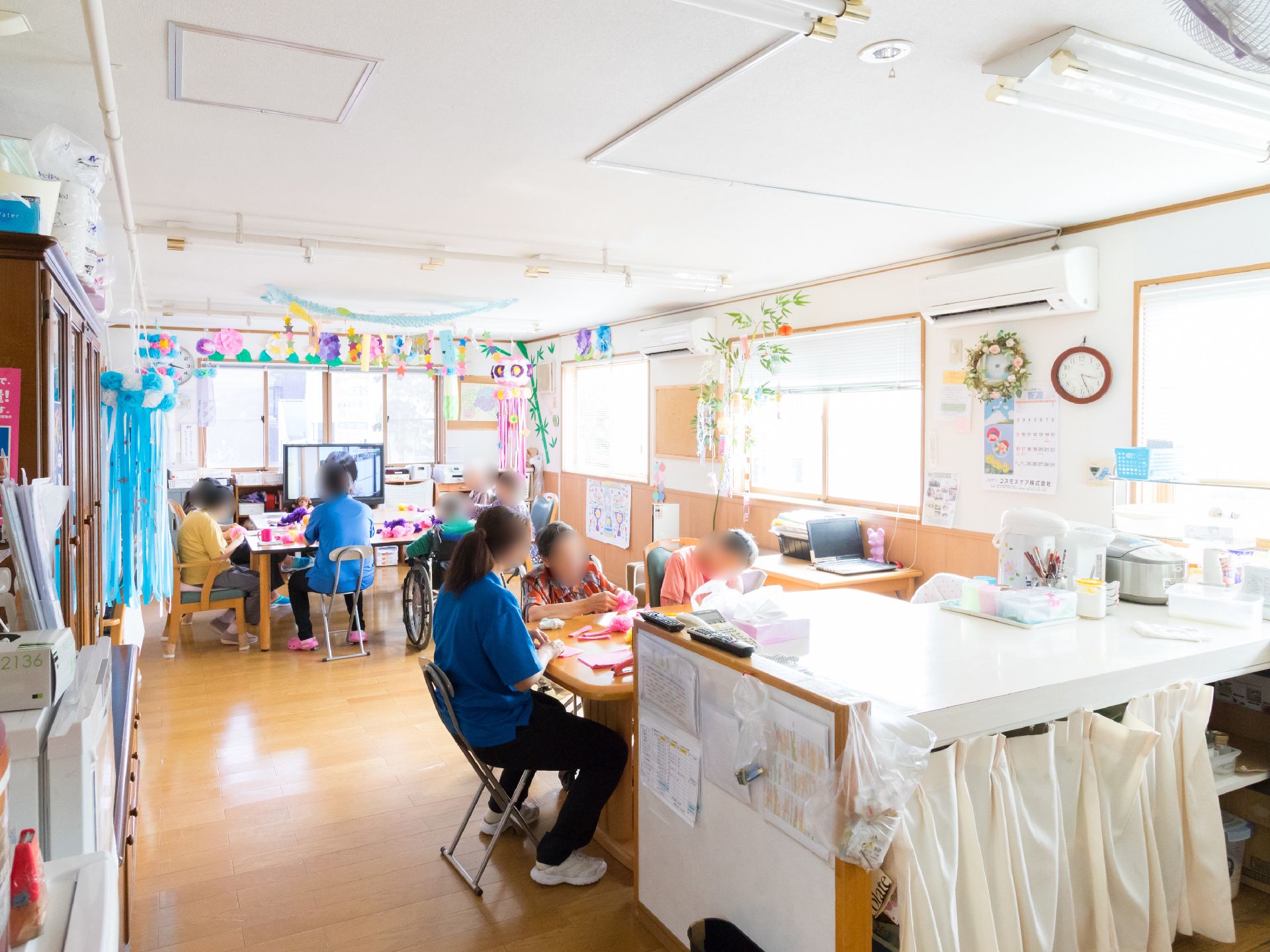 大きな窓があり、よく光が差し込む明るい多目的室。テーブルが２つあり他の入居者と一緒に時間を過ごせる。