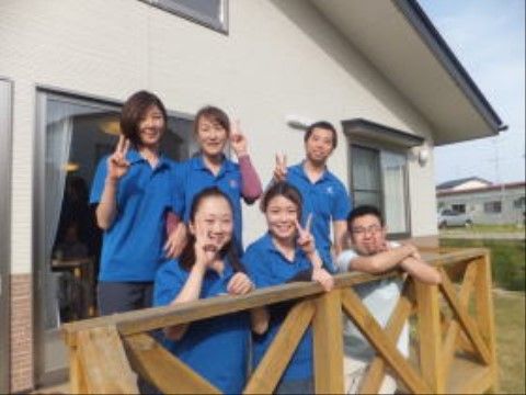 お揃いの青い制服を着て、ウッドデッキでポーズをとるスタッフ