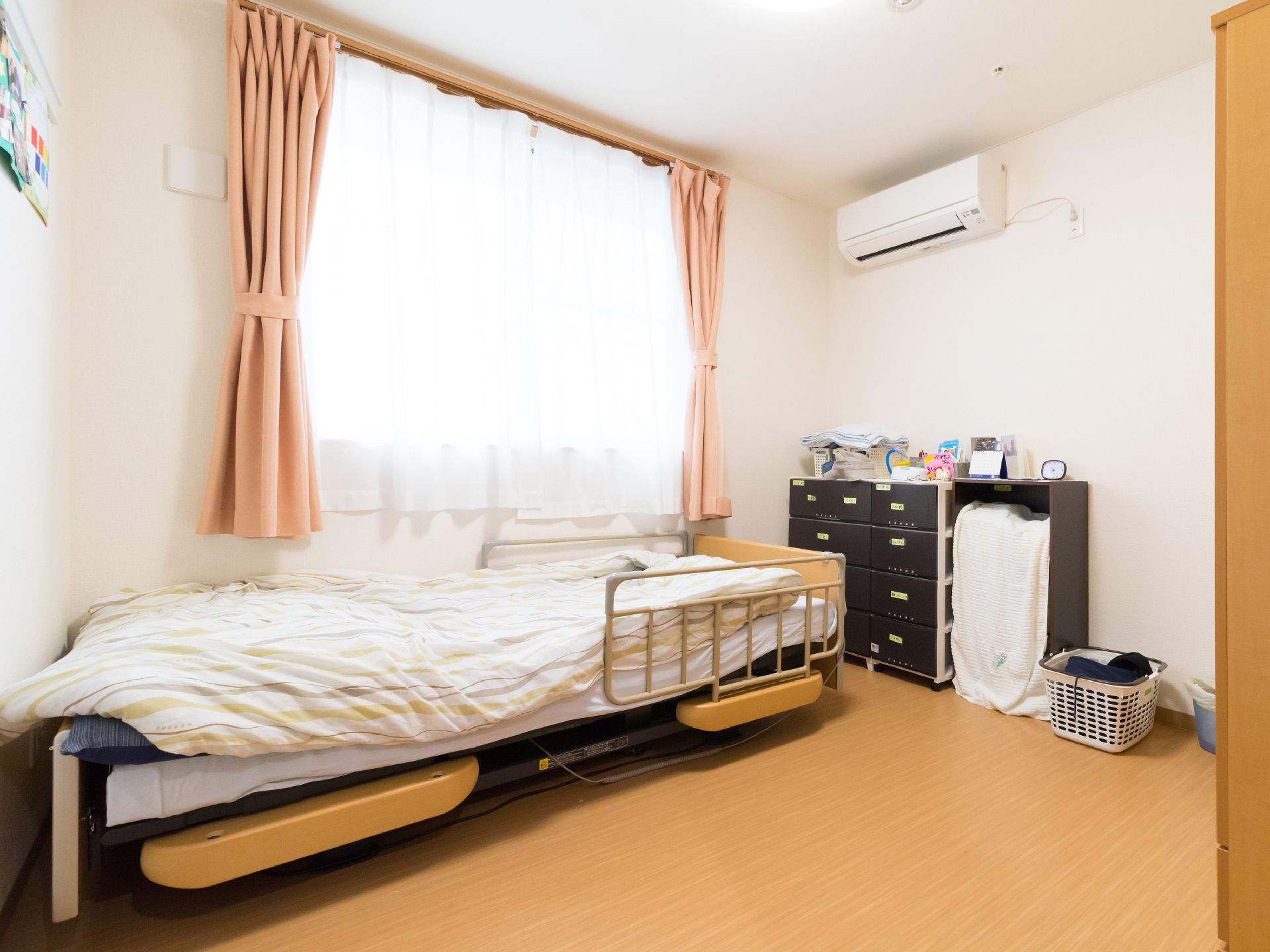 居室の窓からは日が差し込み、カーテンがついている。窓に沿って、手すり付きのベッドが置かれている。エアコンが完備されている。