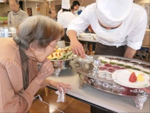 白衣を着て調理を取り分けるスタッフと、それを見る高齢女性