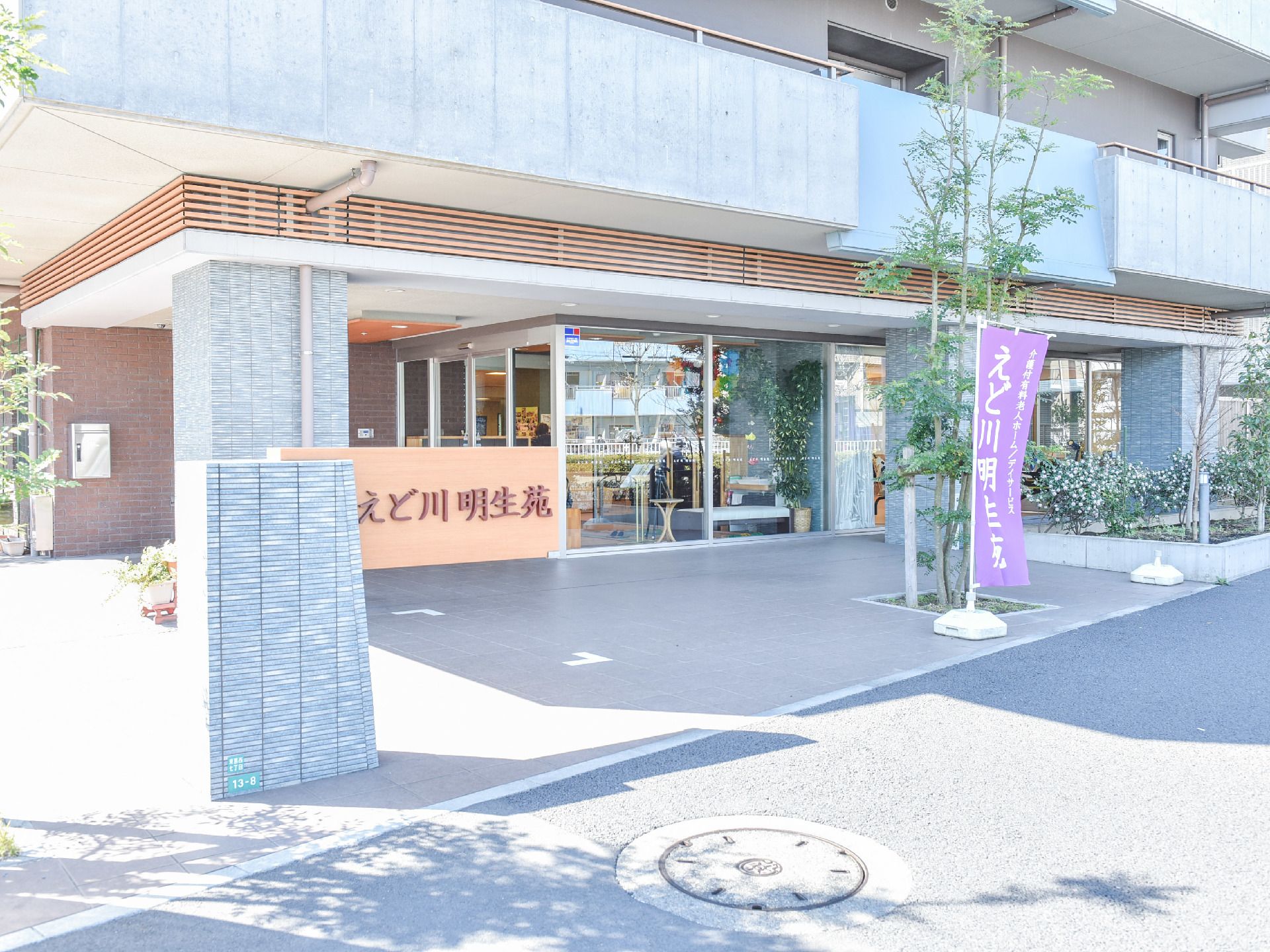 道路側から見た建物外観の様子だ。一階部分はガラス張りになっているようだ。植物も植樹されてグリーンが美しい。