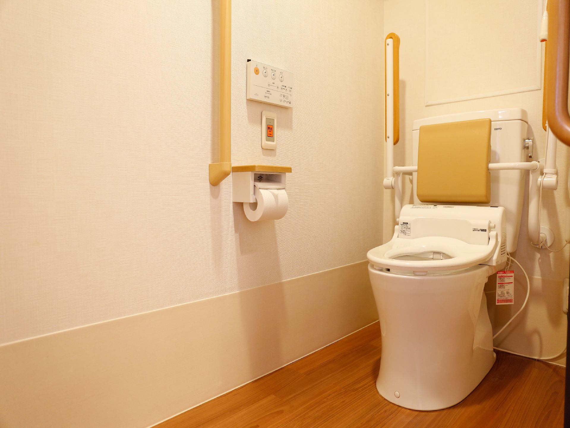 温水洗浄便座を取りつけたトイレで、便座の両側に折り畳み式の手すりが設置されている。手すりは上げられている。