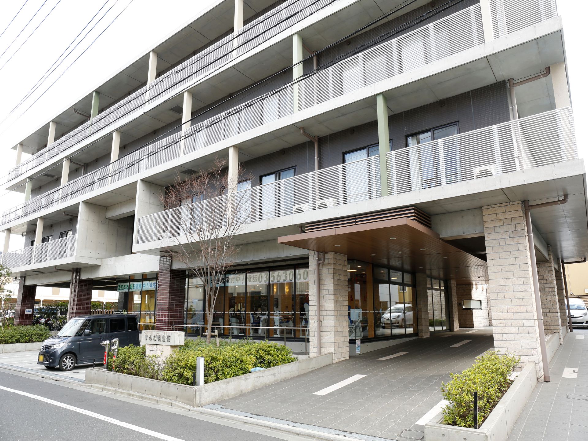 グレーのレンガの柱で支えられた玄関ポーチが施設の下をくぐり、奥にある駐車場へ続いている。3階建てでベランダが並んでいる。