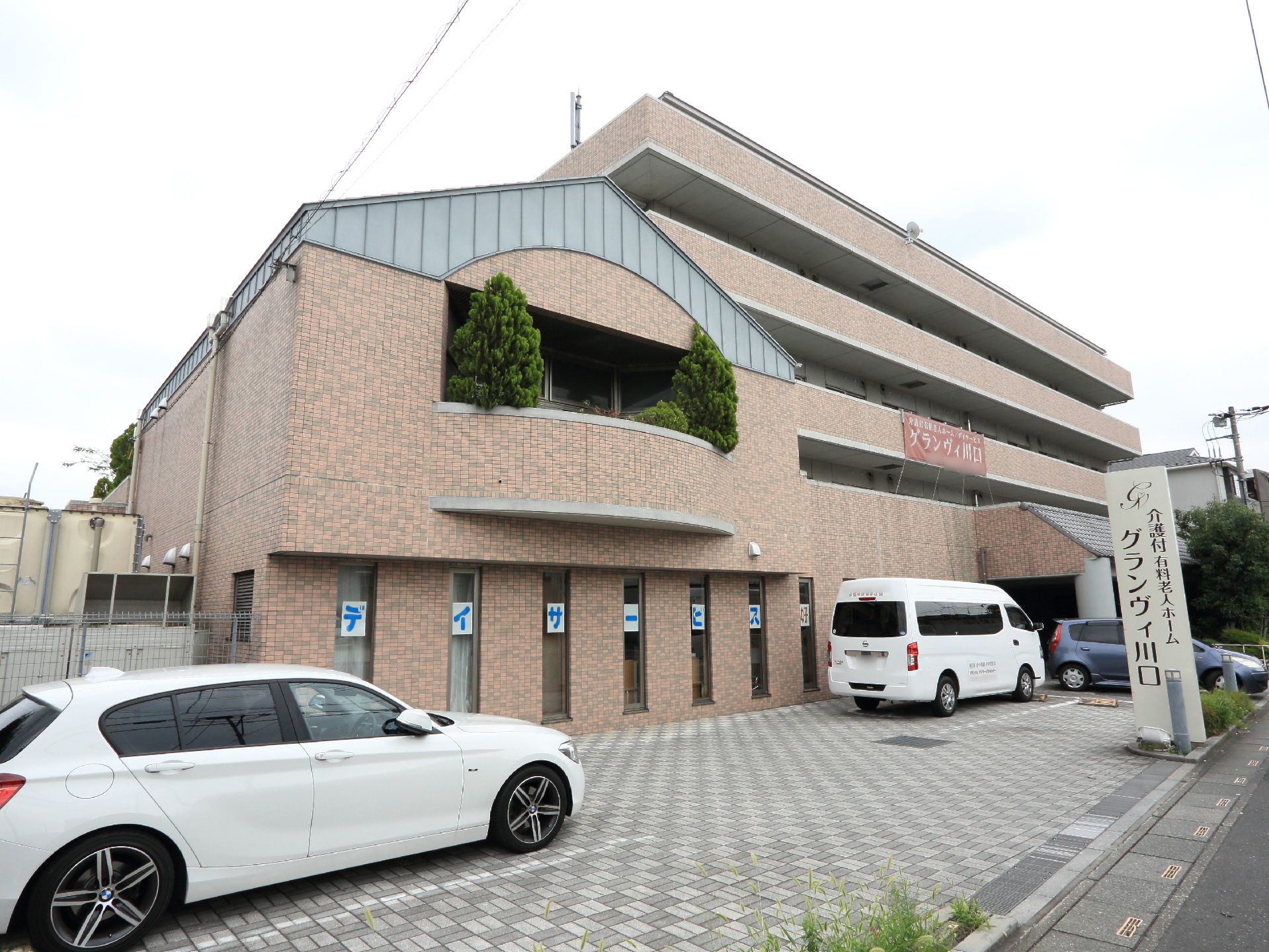 ベージュ色の壁の施設の外観。建物が車道より奥まった所に建っているので、安心できる。周りは静かな住宅街である。