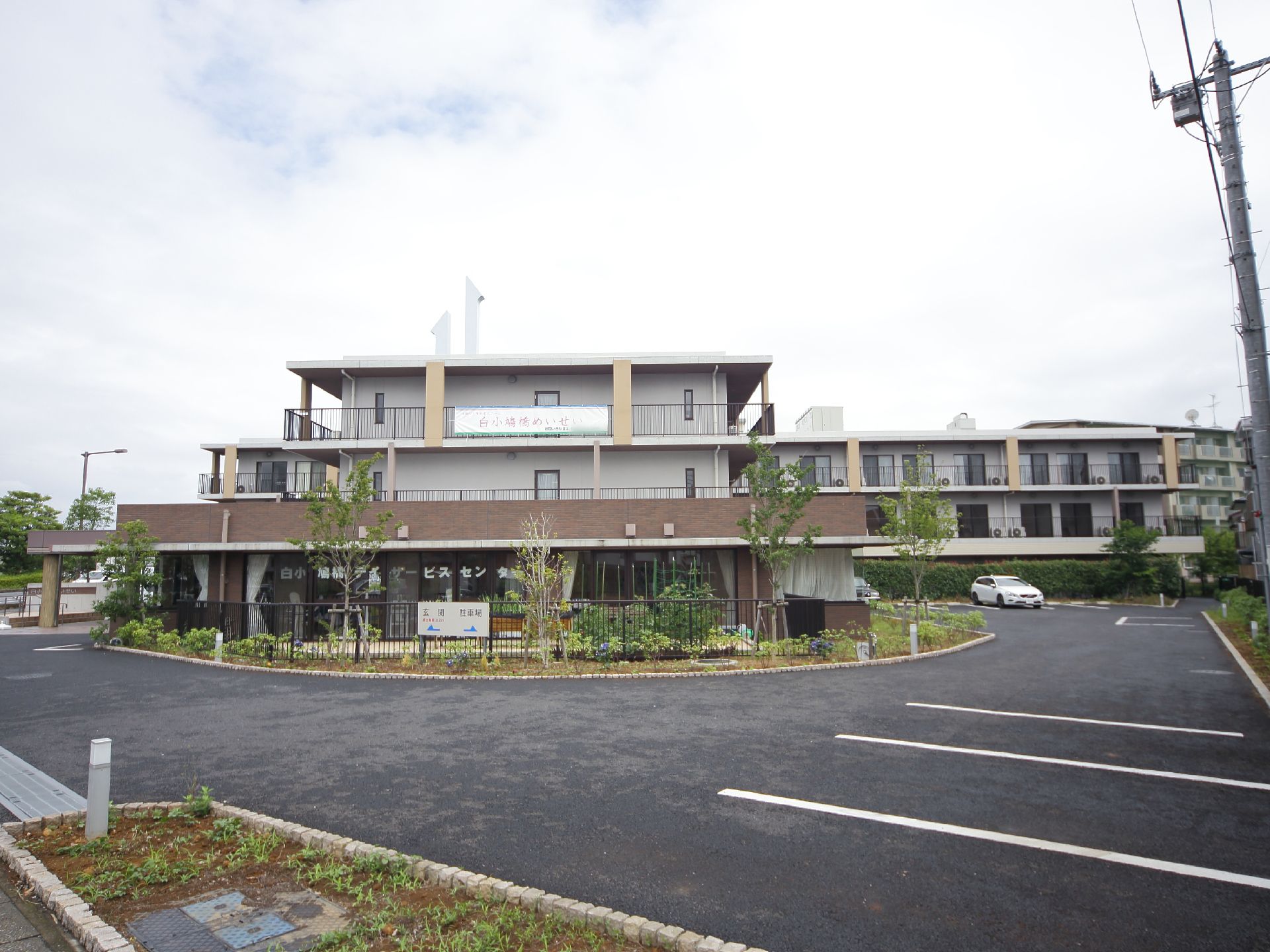 ３階建ての建物で、白とベージュ、茶色を基調にした施設である。建物を囲むように駐車スペースが広がっている。