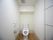 白い壁のトイレで、中央に温水洗浄便座が設置されている。操作パネルとトイレットペーパーが壁に取りつけられている。