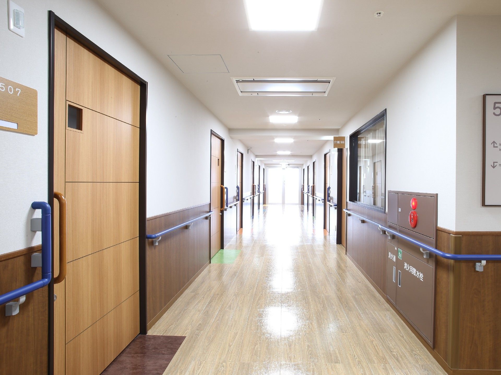 きれいに磨かれたフローリングの床の通路である。両側の壁に手すりが設置され、たくさんのスライドドアの入口がある。