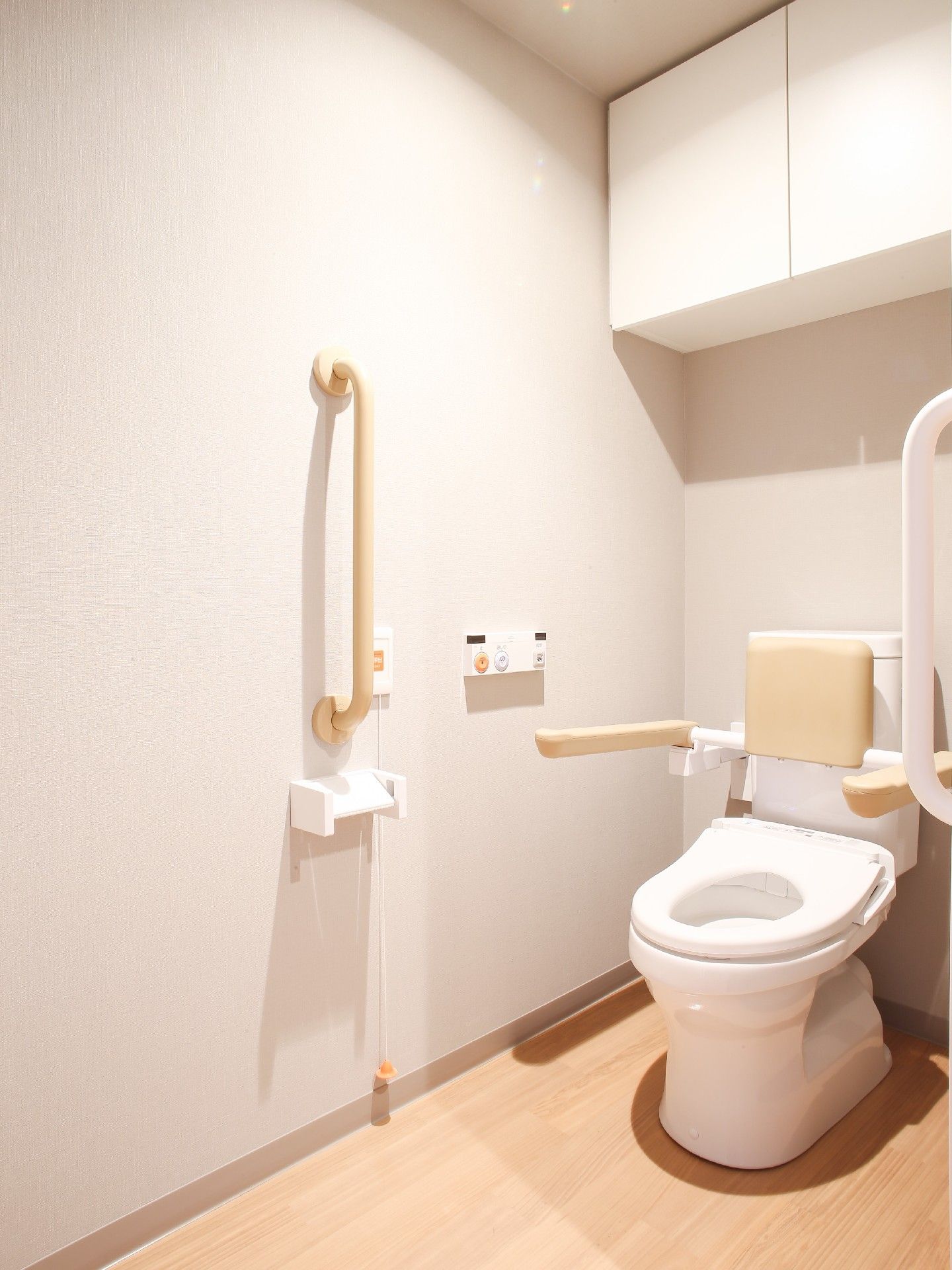 白いタンクがついた洋式トイレがあり、便座のふたが取っ払われている。便器にはクリーム色の背もたれが設置されている。