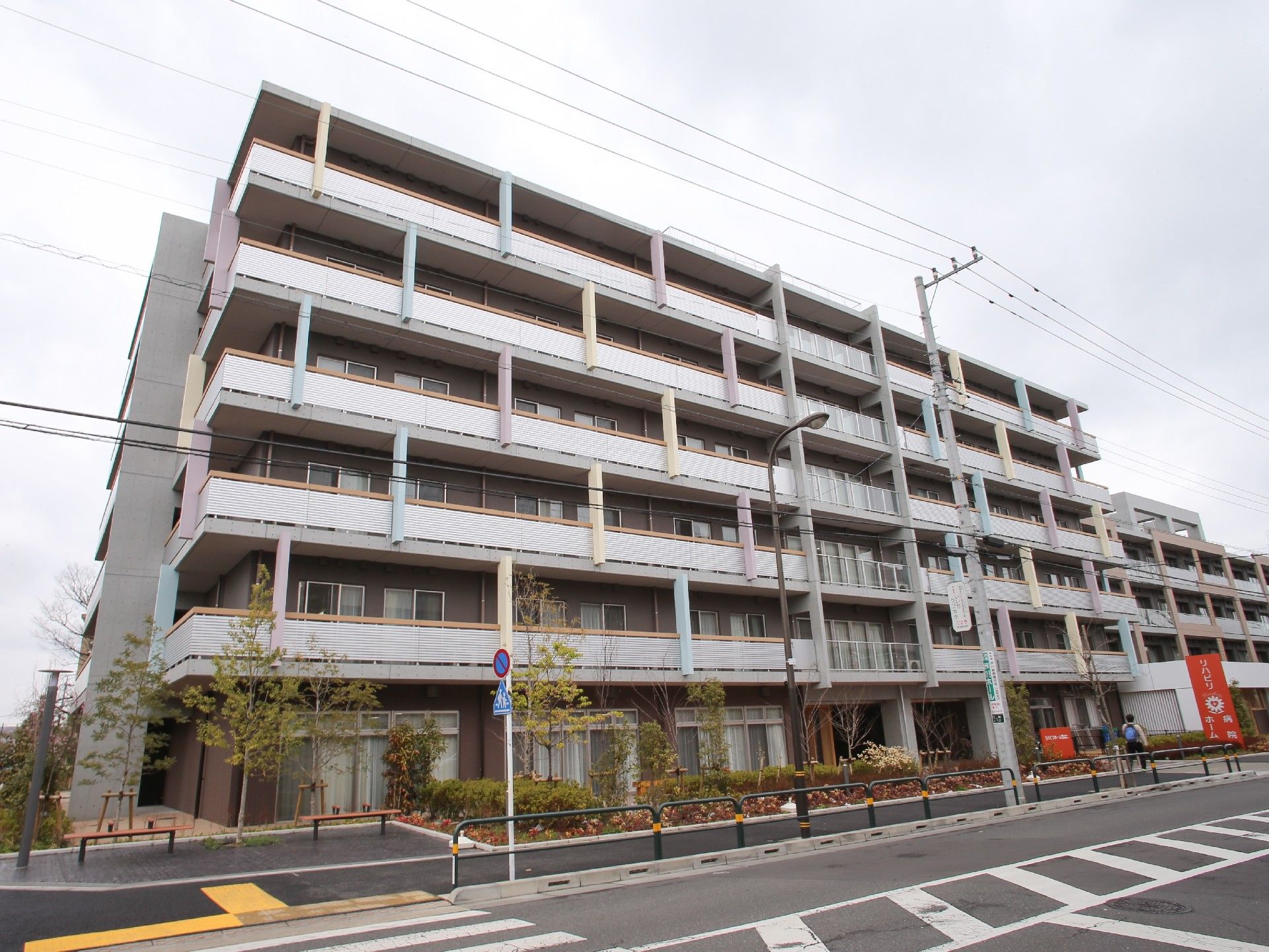 ６階建ての大きなビルのような建物が建っている。建物の前は点字ブロックが設置された広い歩道と横断歩道がある。