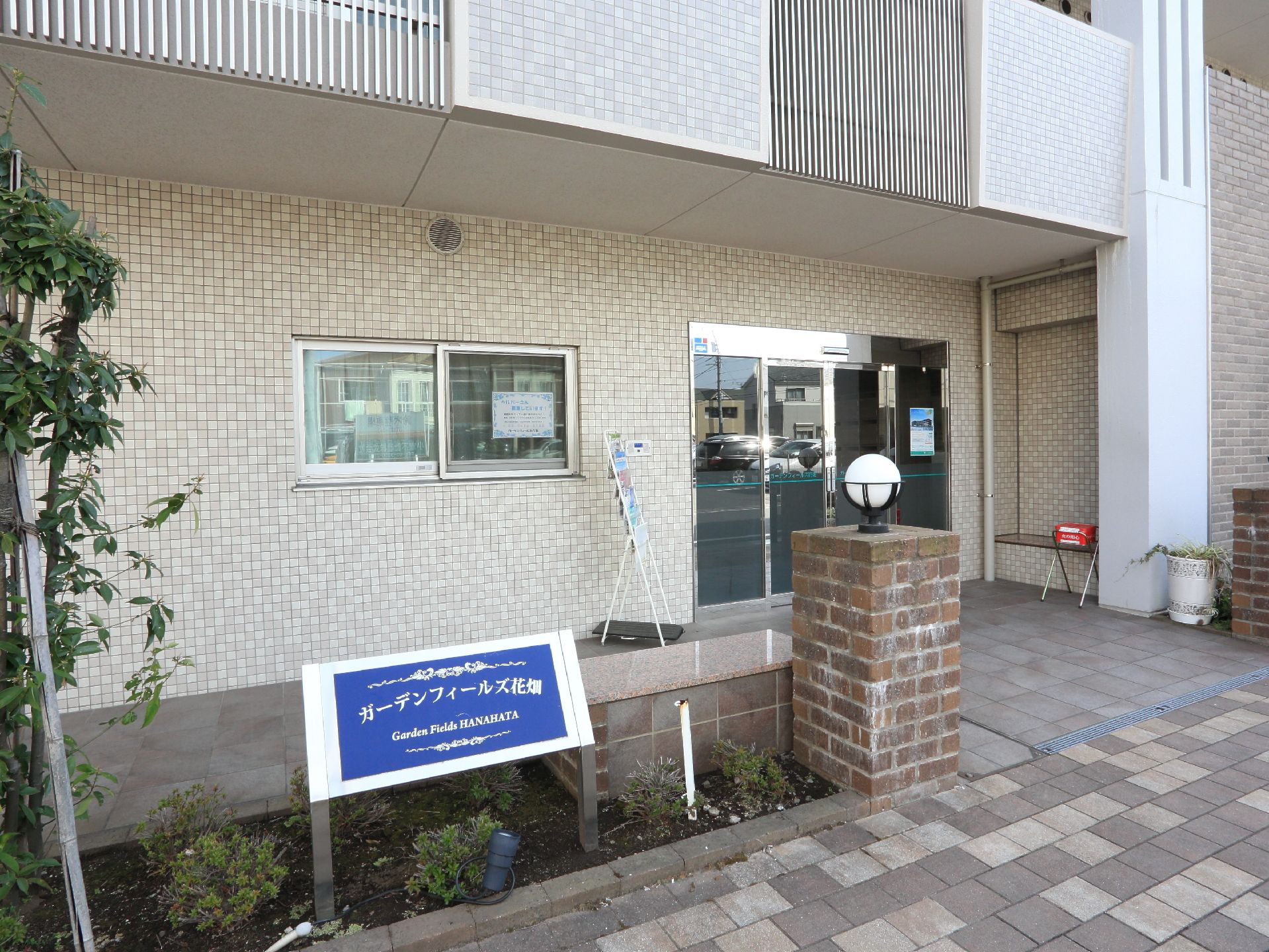 施設の入口は、高級感がありおしゃれな雰囲気。花壇があり、植物が植わっている。玄関外には、座るスペースもある。