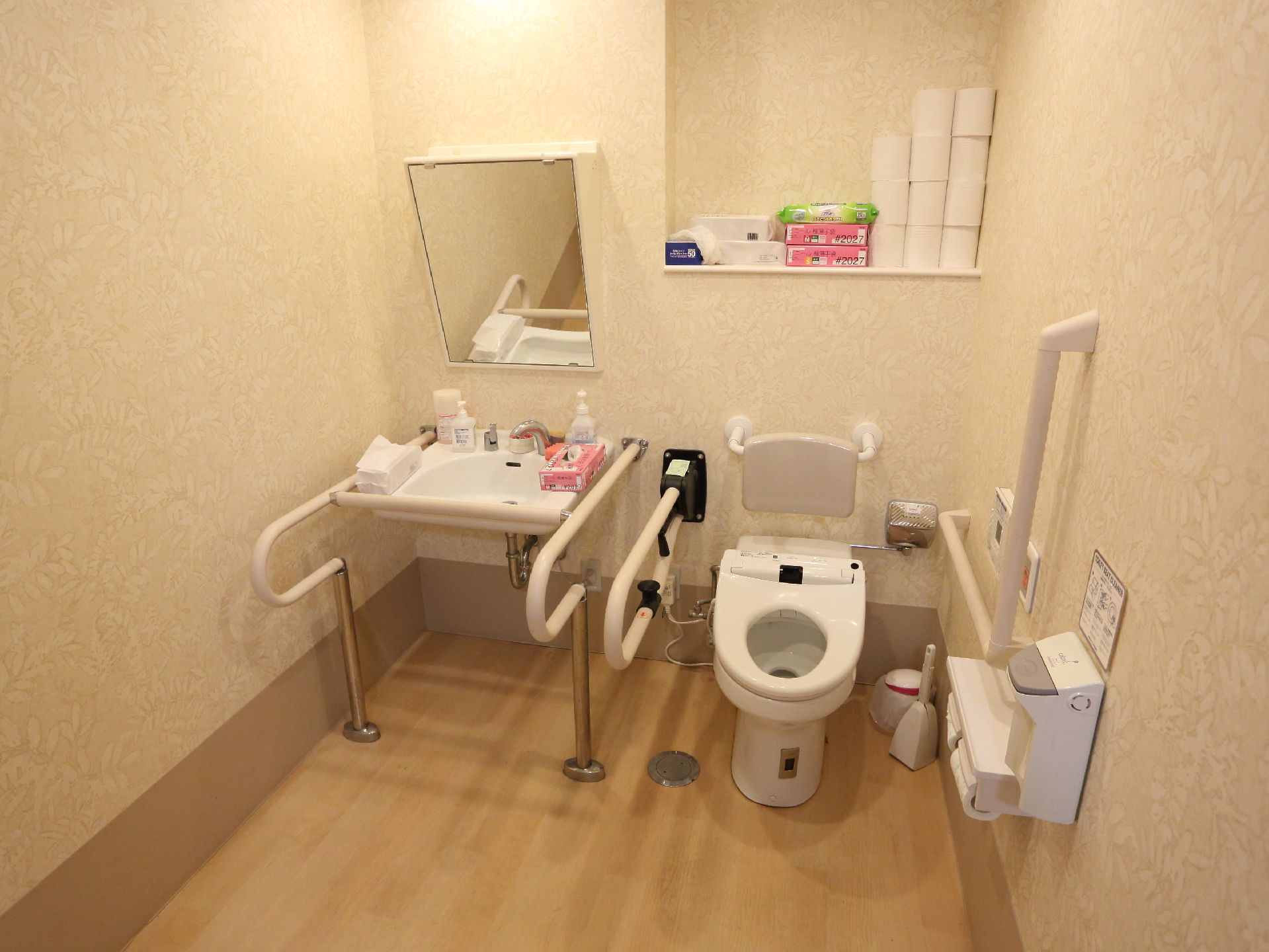 施設内にある、トイレと洗面台がひとつになったタイプの個室トイレ。トイレ横と洗面台横には、手すりが設置されている。