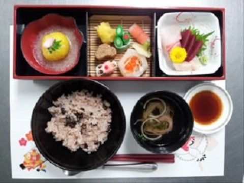 鶴の描かれた和風のテーブルマットに刺身や煮物、ご飯と味噌汁が並んでいる