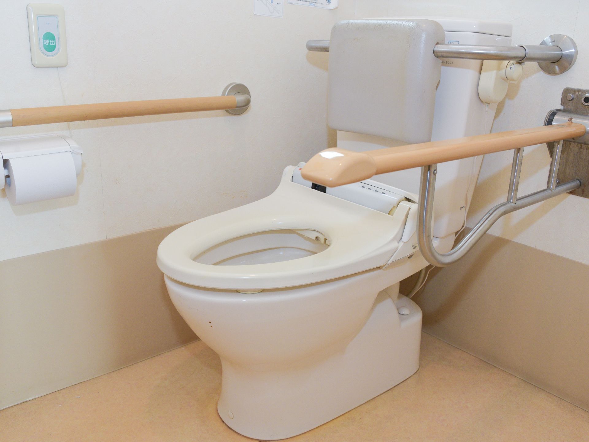施設内のトイレに固定式の手すりと、可動式の手すりがついている。タンク部分には背もたれがある。ナースコールもあるので安心。