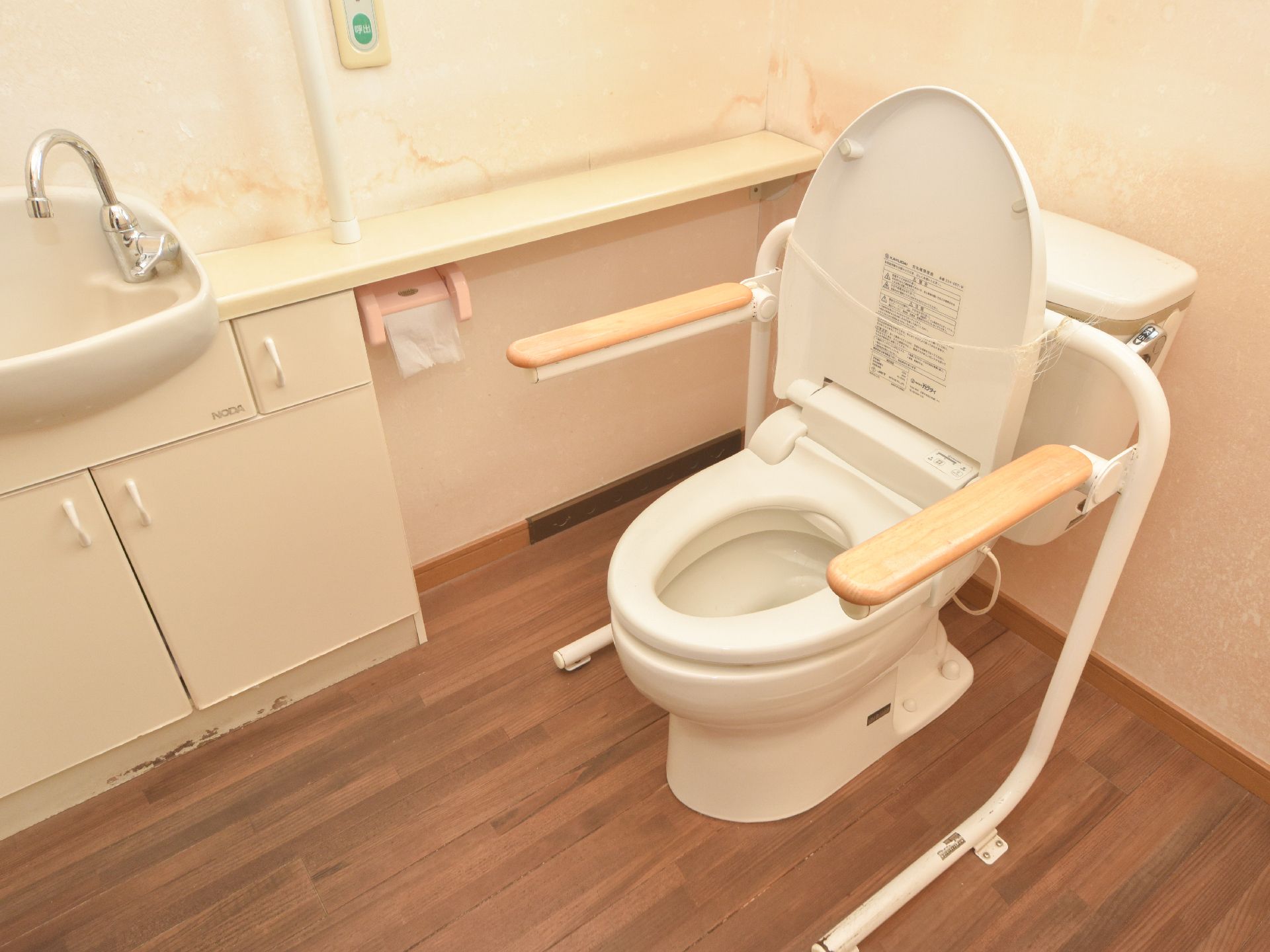 清潔で、とても広い部屋に、様式便器と洗面台が設置されている。便器には可動式の手すりが取り付けられている。