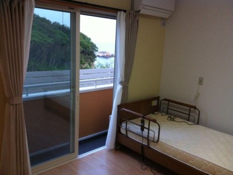 部屋の窓からの眺めが良く、海や緑が見える。室内には介護用のベッドが1台置かれ、壁にエアコンが付けられている。