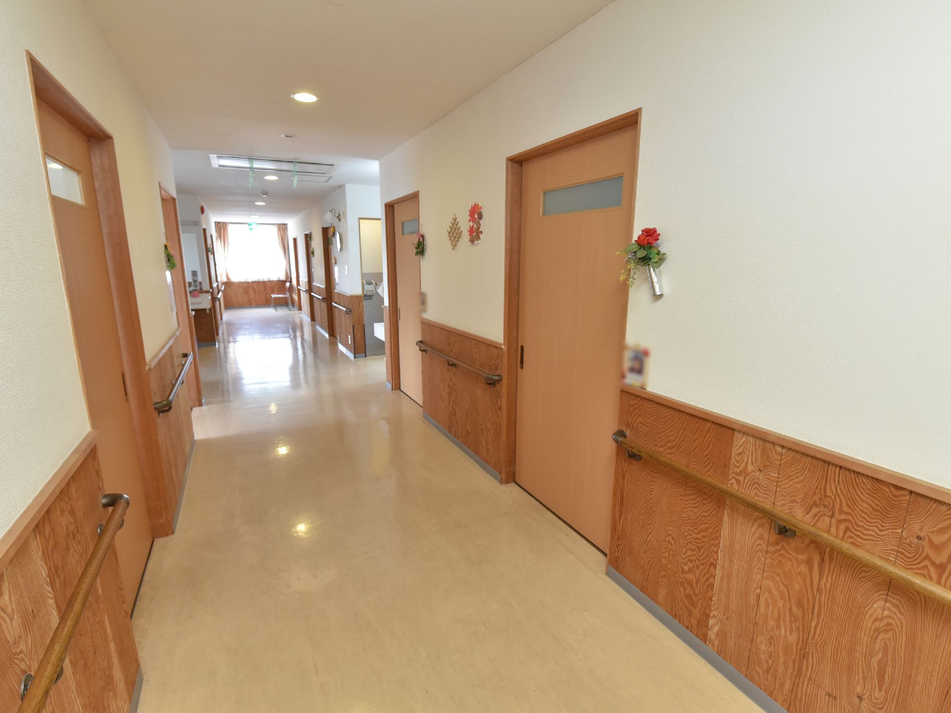 廊下の突き当たりに大きな窓があり、両側に居室の入口扉が並んでいる。また、壁には手すりが設置され、花や飾りが飾られている。