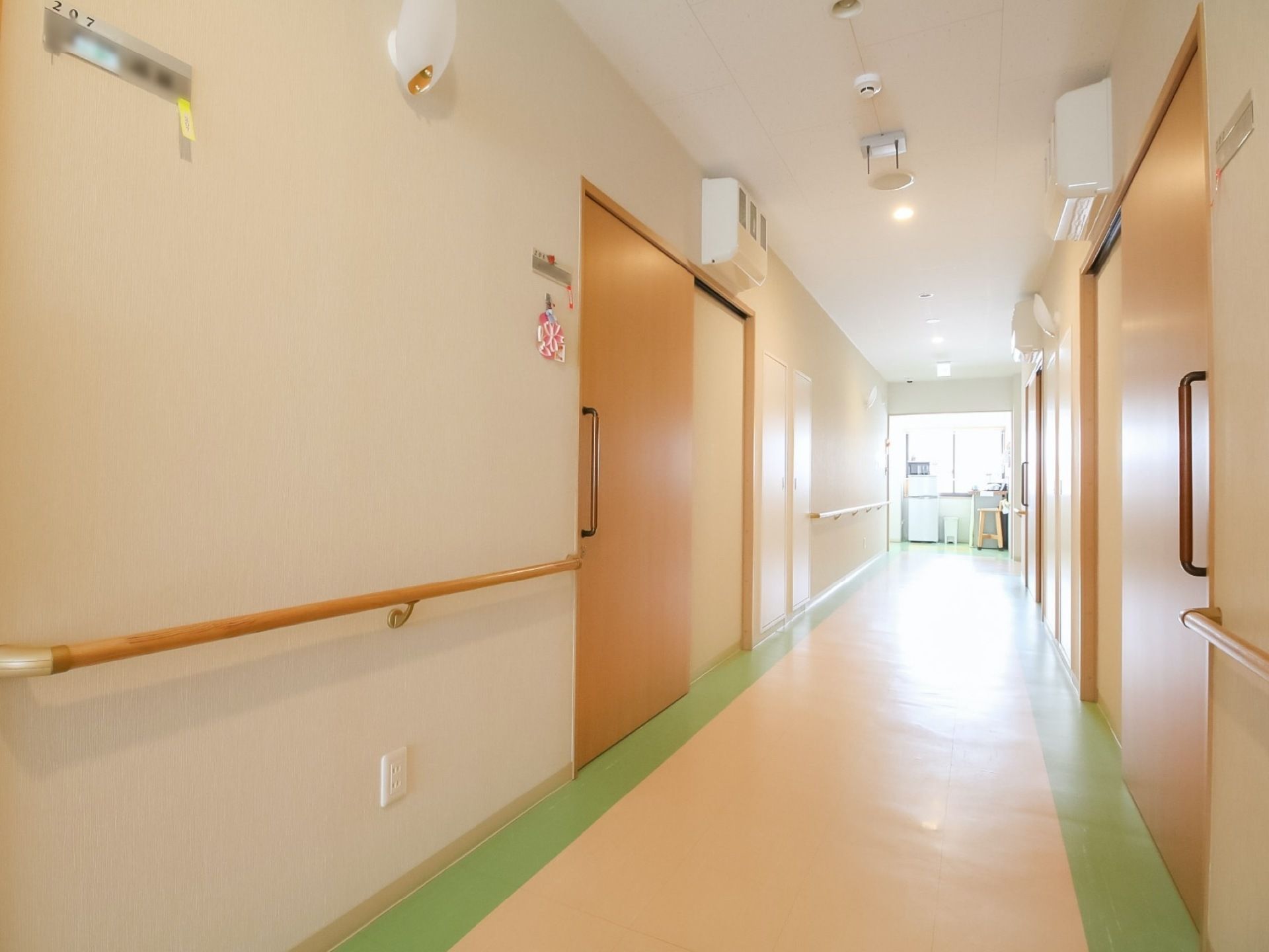両側に居室のドアが並んでいる廊下がある。壁には手すりが設置されており、突き当りには窓があり、自然光が差し込んでいる。