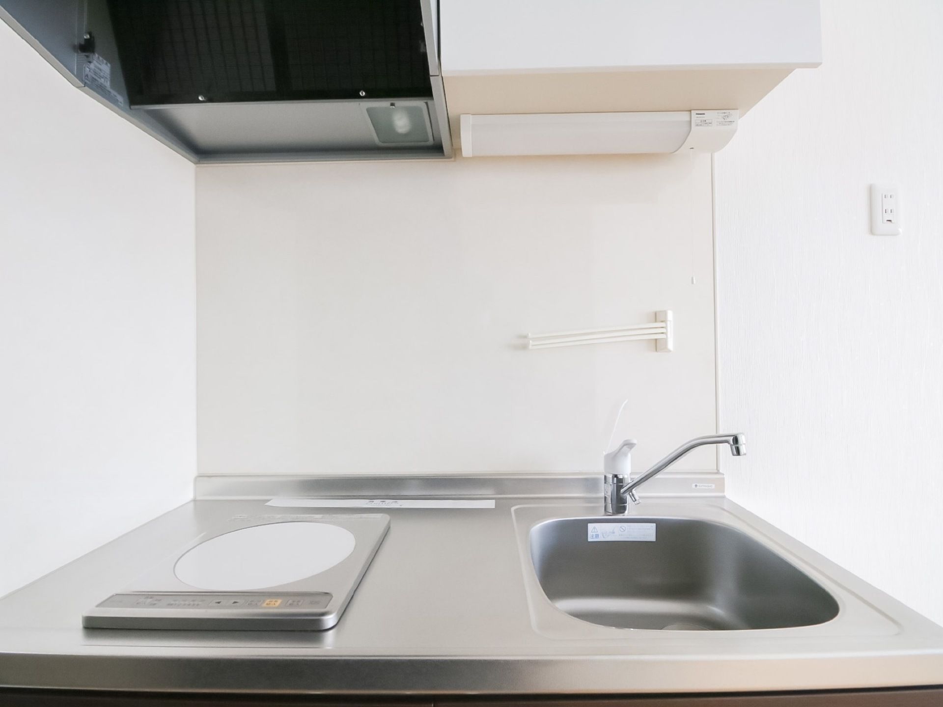 居室にあるミニキッチン。電熱ヒーターが１つあり、大きな換気扇が付いている。流し台の上には照明器具が付いている。