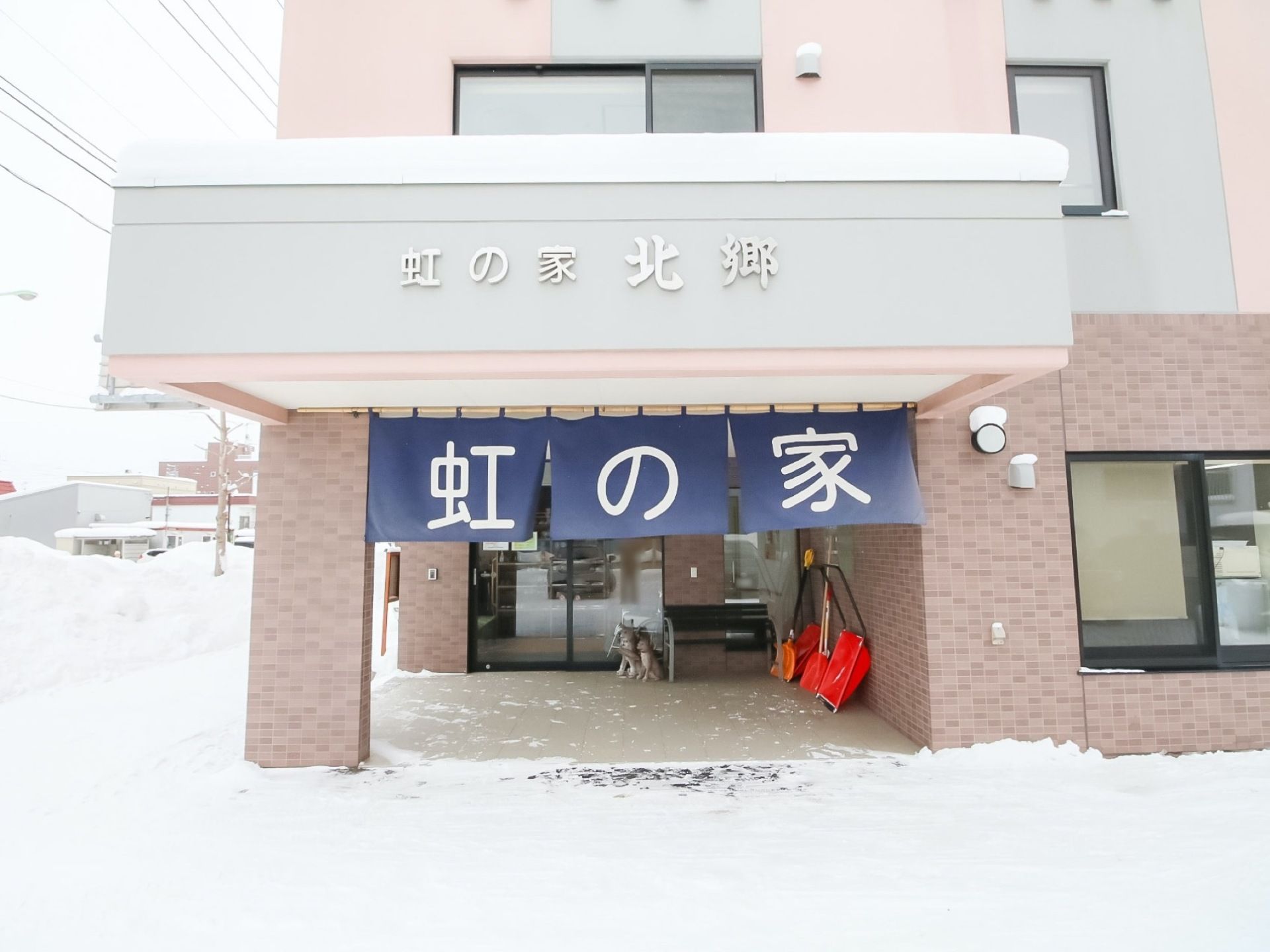 モザイク調のレンガのタイルに囲まれた玄関がある。ガラス張りのドアがあり、建物の側面には施設名が書かれている。紺色の暖簾が掛かっている。