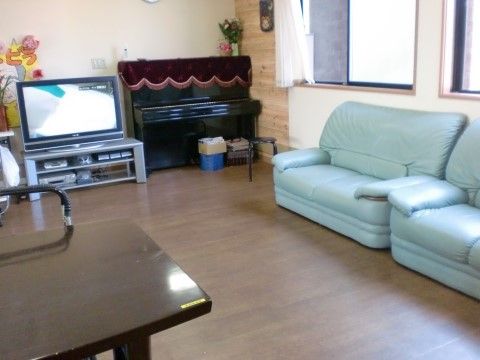 テレビの横にピアノが置かれている。窓の側には緑がかったソファも２脚見える。テーブルもありゆったりとできるスペースとなっている。