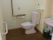 出入口とトイレットペーパーホルダーのサイドに手すりが取り付けられているトイレ。洗面台やゴミ箱も設置されている。