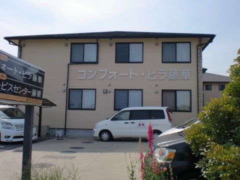 広い駐車スペースを備えた、ベージュの外壁の施設外観