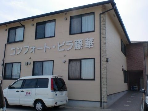 正面に施設の名称が大きく書かれた壁がある。手前には車椅子も乗せられる自動車が置かれている。奥まで続くスロープもある。