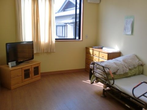 車椅子をご利用の方でも生活しやすいフローリングの居室である。介護ベッドや収納家具、テレビが置かれている。