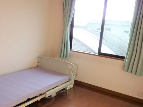 大きな窓から外の景色がよく見える部屋である。緑のカーテン、フローリングの床で気分が落ち着く。電動ベッドも完備されている。