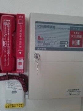 白いボックスと赤い受話器がセットになった火災通報装置がある。ボタンを強い力で押すだけで消防署に通報できる。
