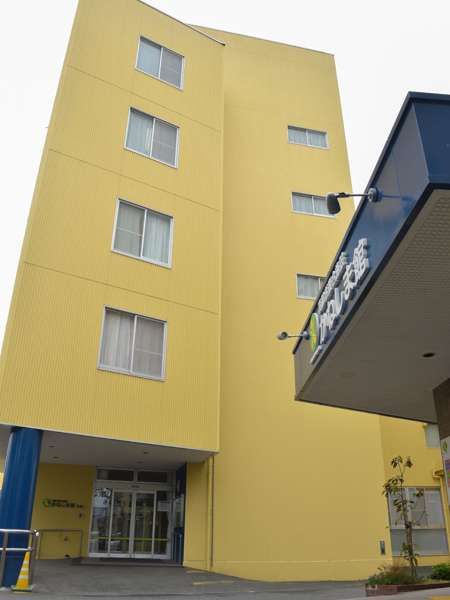 施設は5階建ての建物である。壁面には四角い窓が複数あり、それぞれに白いカーテンが掛けられている。青い柱がある。