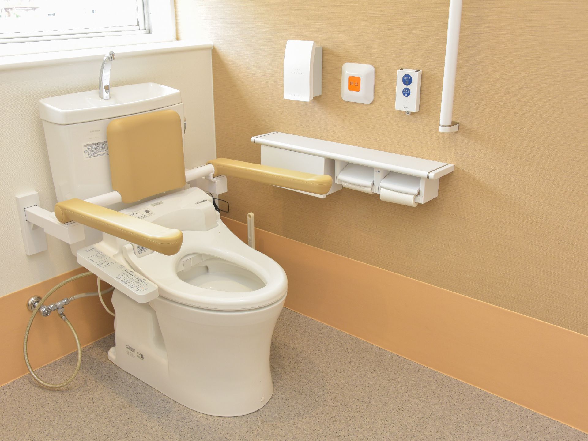 トイレには壁に設けられた窓から日差しが射し込んでいる。右側の壁には手すりがあり、その左にナースコールがある。