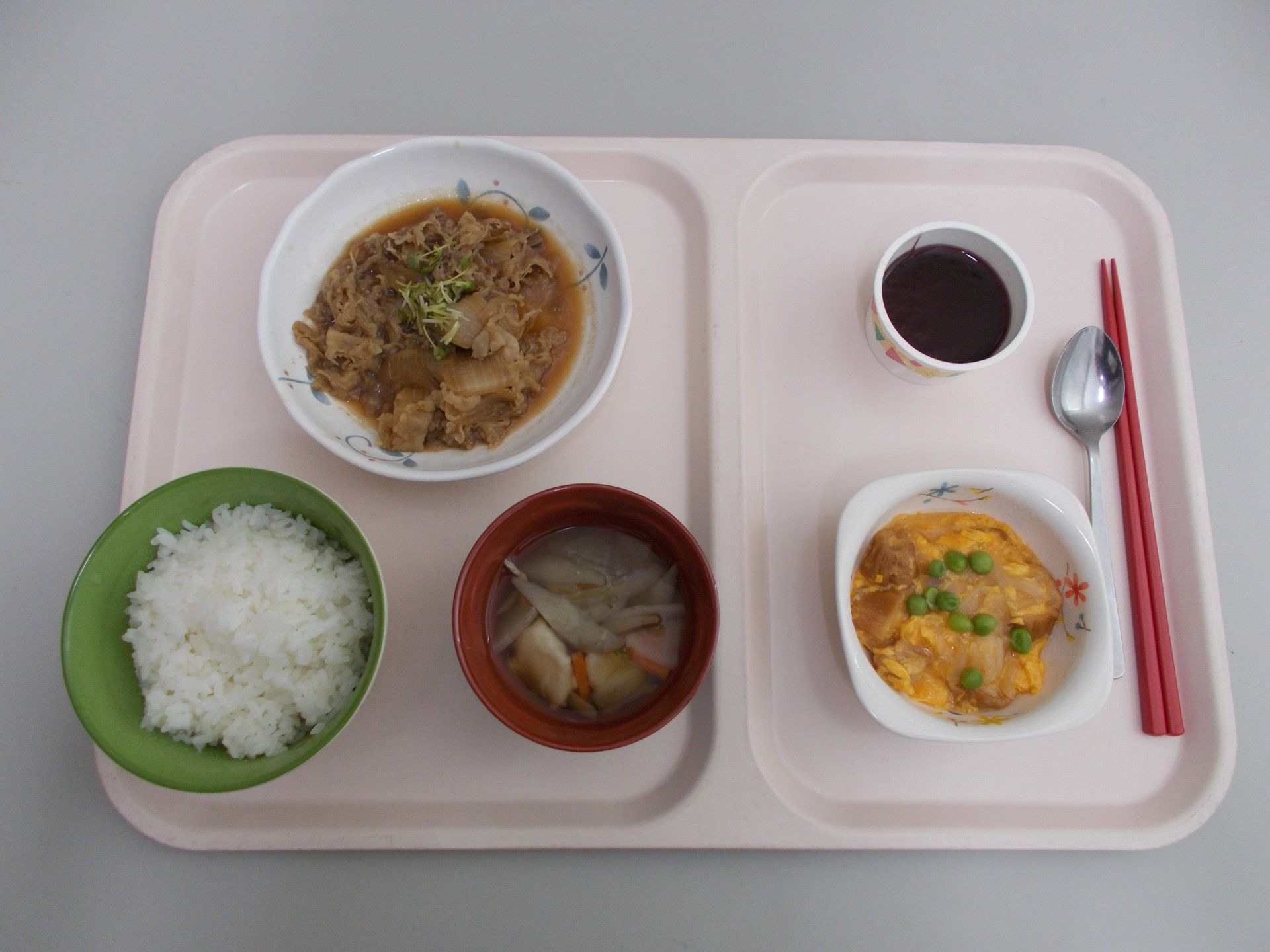 黄色いトレーの上に1人分の食事がセットされている。右側の手前に赤い箸がセットされ、ご飯や味噌汁などの器が並んでいる。