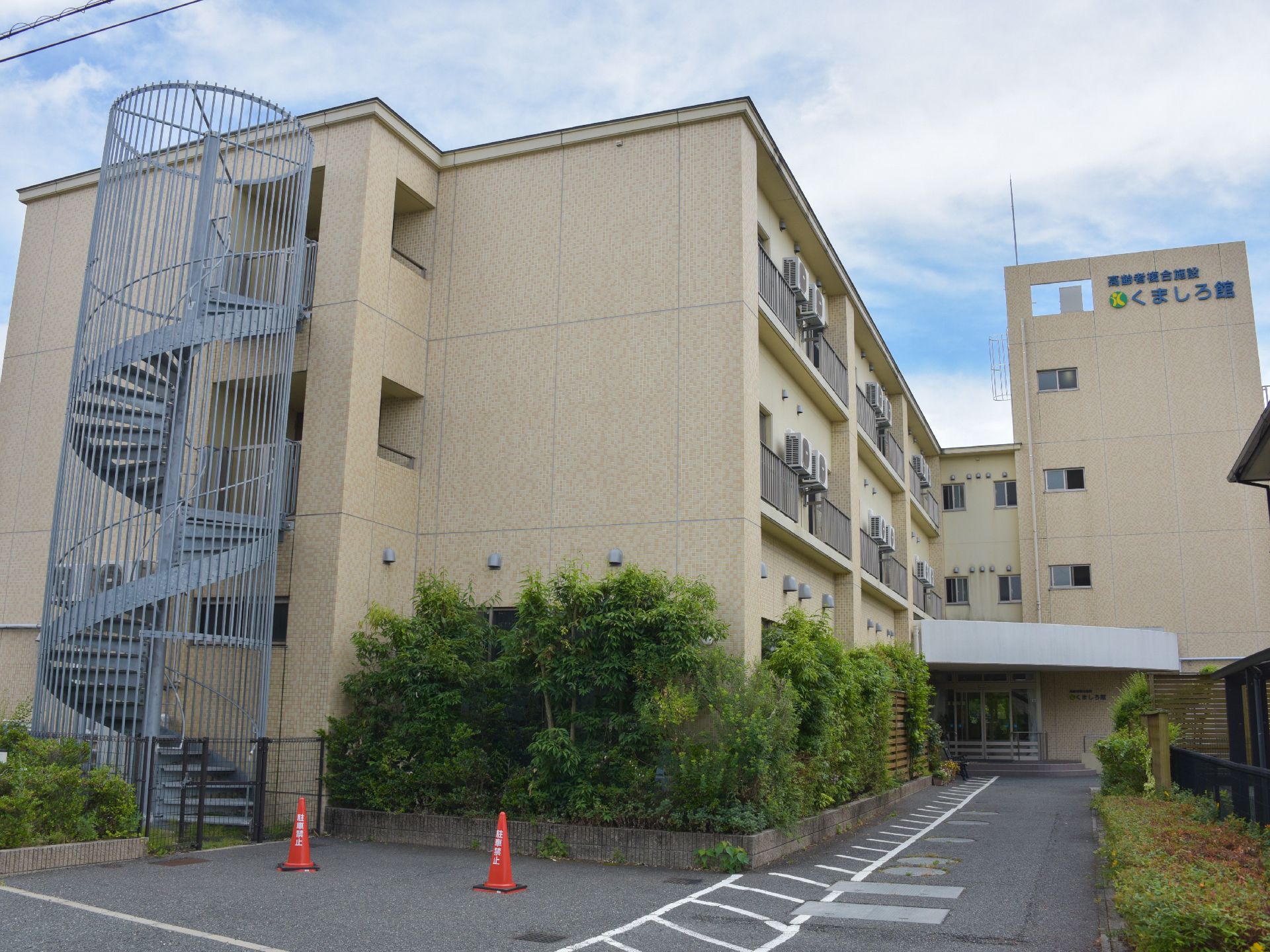 施設は3階建ての建物で、左側の壁にはらせん状の外階段が設置されている。建物の壁際には背の高い木が植えられている。