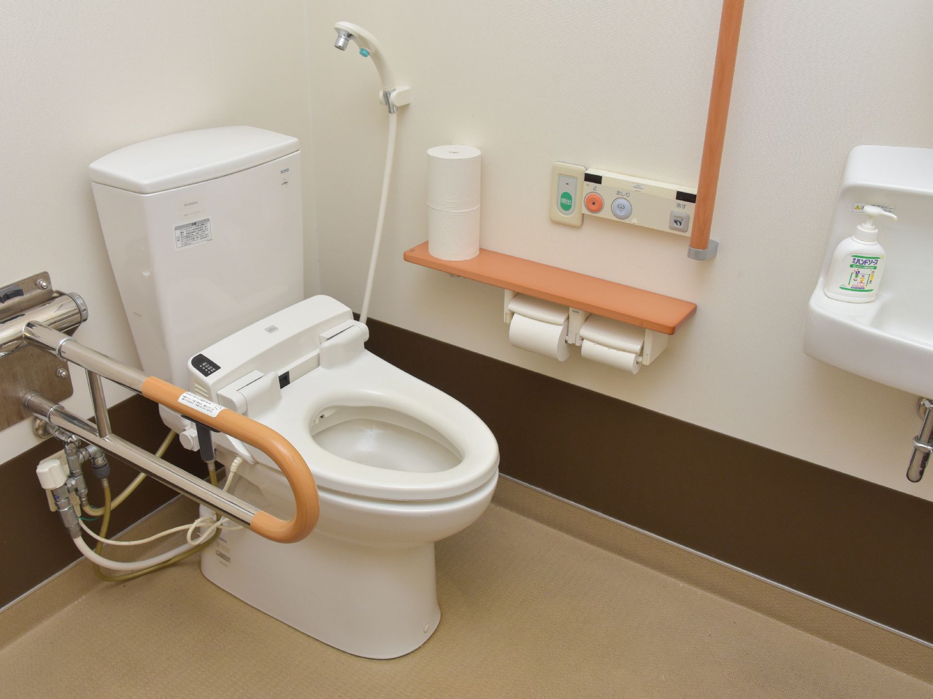 トイレは温水洗浄便座付きで、操作パネルは右側の壁に設置されている。その右には手すり、左にはナースコールがある。