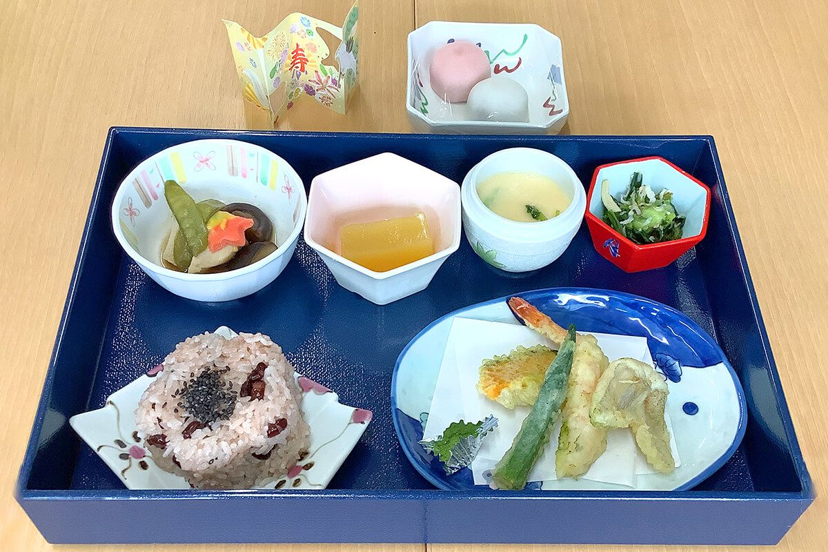 1人分の食事が黒いトレーの上にセットされている。ご飯と汁物のほかにおかずが3品あり、デザートが2品添えられている。