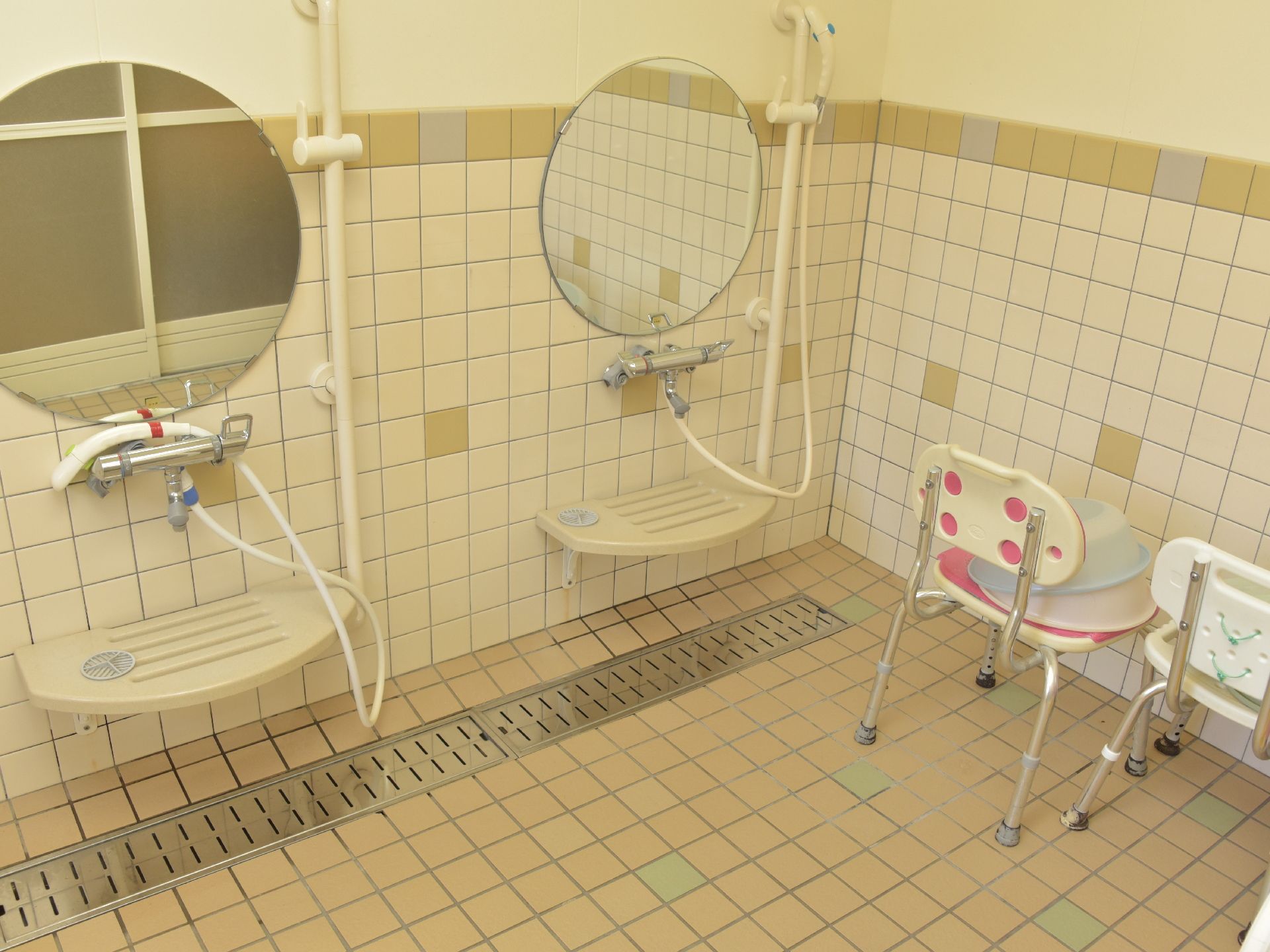 シャワー横には安全の為、手すりが備え付けられている。足腰に不安がある方でも座って洗えるように背もたれ付きの風呂椅子が用意されている。