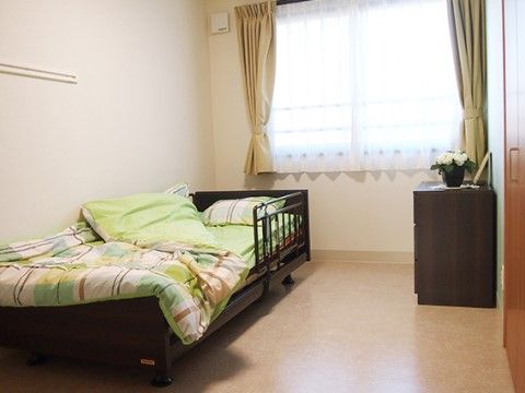 居室の壁には衣紋掛けが設置してあるので、衣類などが掛けられて便利である。可動式のベッドに柵をつけ、安全にそして無理なく寝起きしている。