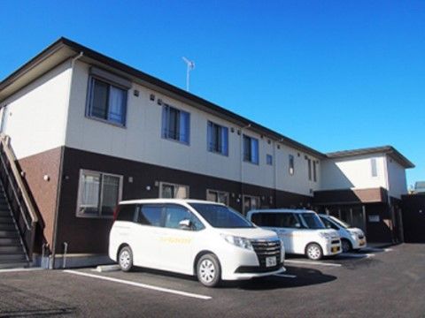 ブラウンとホワイトのコントラストが鮮やかな２階建ての建物である。通常の集合住宅のような雰囲気で、建物の前には駐車場がある。