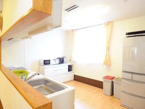 キッチンスペースには大きな窓があり、床はフローリングになっている。システムキッチン、冷蔵庫、収納家具が置かれている。