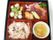朱色と黒の重箱に、黒ゴマが乗ったおこわ、刺身、煮物、デザートが並んでいる。見た目も美しく、特別感がある華やかな食卓になっている。