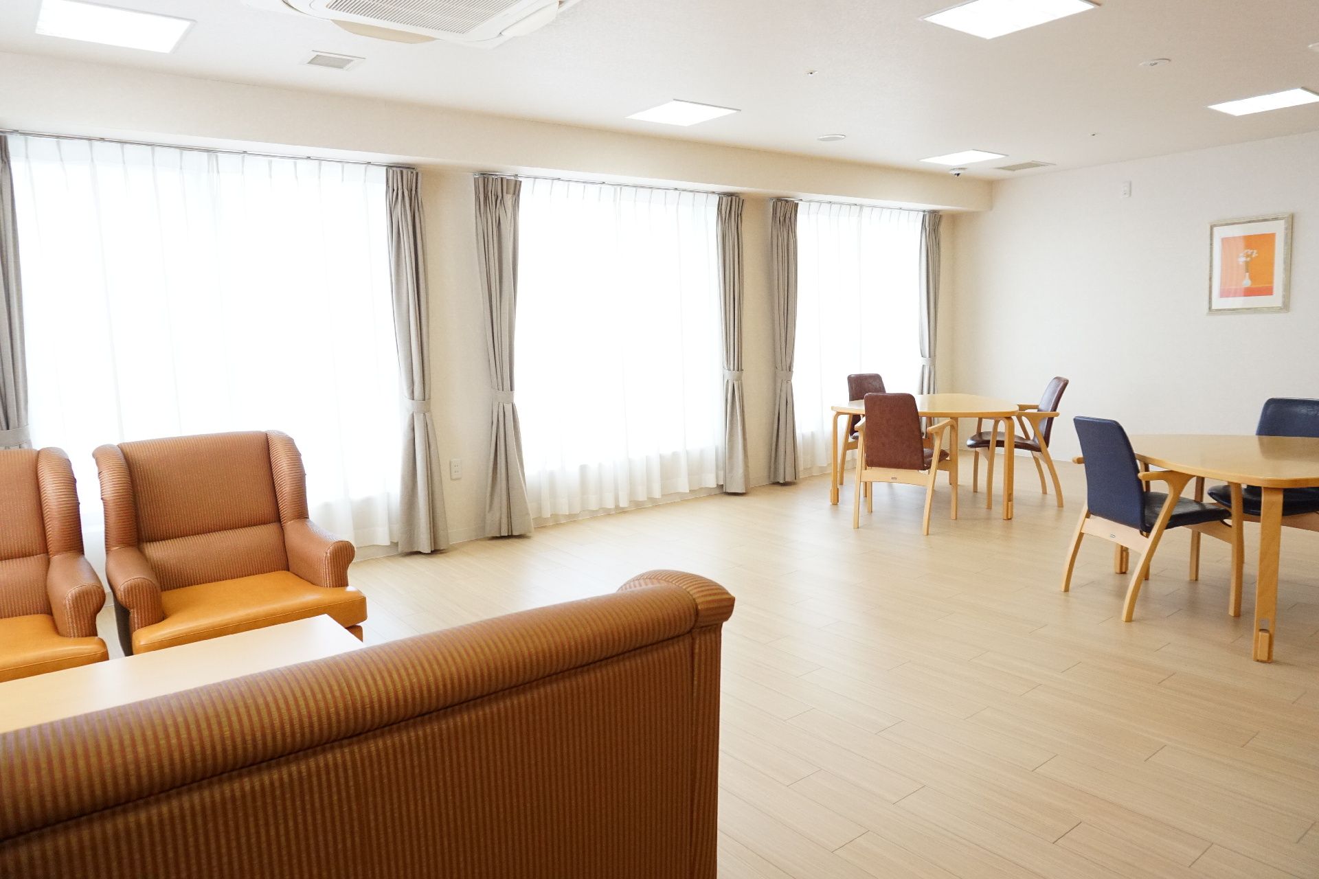 大きな窓から陽光が降り注ぎ、テーブル、椅子が置かれているリビング