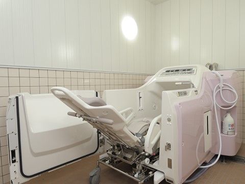 白い壁の浴室で、照明が明るく照らしている。お体の不自由な方でも湯船に入ることができる特殊な浴槽が、壁際に置いてある。