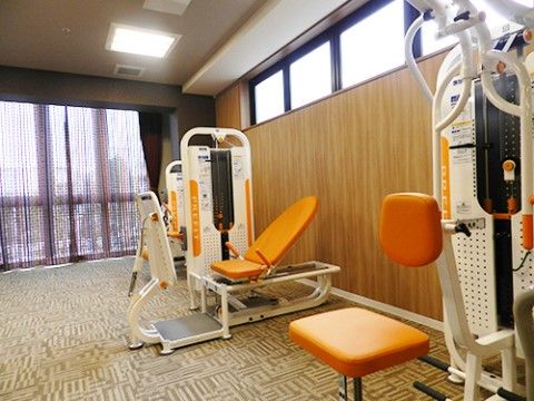 窓が大きく取り付けられていおり、紫色のレースカーテンが付いている。木目の壁の近くには、トレーニングできる器具が置いてある。